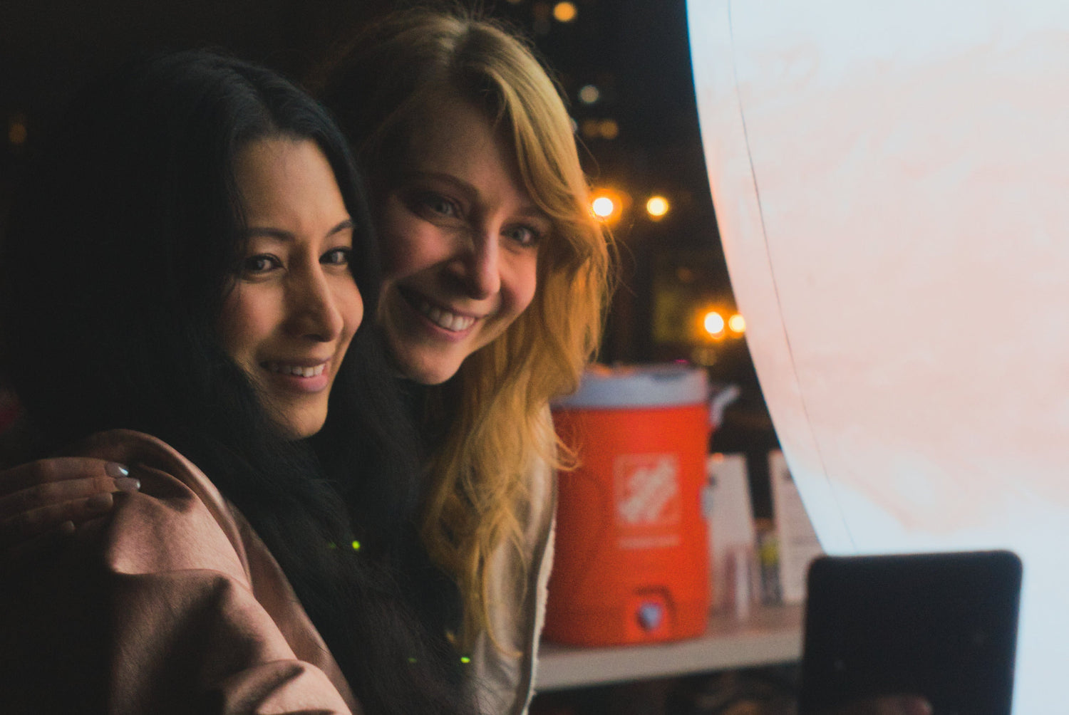 Two women taking a selfie with a tablet at night.